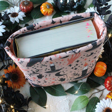 Load image into Gallery viewer, A large-sized Cozy Occult book sleeve is standing on its own, with a hardcover book called "Kingdom of Ash" by Sarah J. Maas within. In the background are black and white flowers, small pumpkins, and leaves.