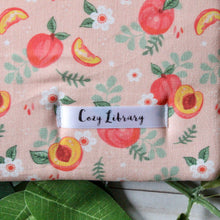 Load image into Gallery viewer, A close up of the Cozy Library tag is shown sewn into a Just Peachy book sleeve.