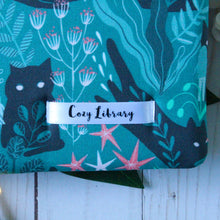 Load image into Gallery viewer, A close up of the Cozy Library tag is shown on the bottom right corner of a Green Forest Guardian book sleeve.