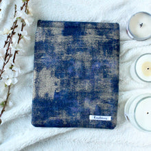 Load image into Gallery viewer, There is a blue, indigo, and gold dust fabric that makes Indigo Gold Dust book sleeve. There are white flowers on the left side of the photo. On the right side, there are three white candles in 3 various sizes on the right side of the picture.
