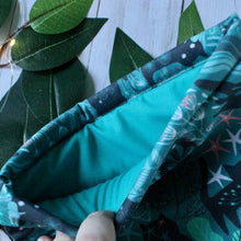 Load image into Gallery viewer, A finger is holding open the Green Forest Guardian book sleeve. With in the book sleeve a turquoise-esque inlay fabric, matching the green of the outer fabric.