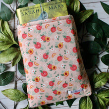 Load image into Gallery viewer, A hardcover book sits within a large-sized Just Peachy book sleeve.There are green leaves in the background.