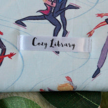 Load image into Gallery viewer, A close up of the Cozy Library tag is shown on the bottom right corner of a Boys on Ice book sleeve.
