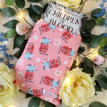 Load image into Gallery viewer, A medium-sized Go Away I'm Reading book sleeve, which has a book titled "Children of Blood and Bone" by Tomi Adeyemi halfway into it. There are flowers and leaves in the background of the photo.