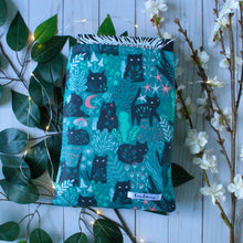 Load image into Gallery viewer, A medium sized Green Forest Guardian book sleeve is pictured. A hardcover book is inside the sleeve. the top of the book is peeking outside of the sleeve. Also pictured are white flowers, green leaves, and a white-washed wooden background. Fairy lights shown give a fantasy-esque feel.