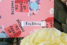 Load image into Gallery viewer, A close up of a Cozy Library tag shown on the bottom right corner of a Go Away I'm Reading book sleeve.