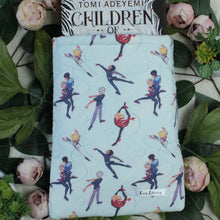 Load image into Gallery viewer, A hardcover book titled "Children of Blood and Bone" by Tomi Adeyemi is shown halfway into a Medium sized Boys on Ice book sleeve. The fabric design of the sleeve shows YOI anime characters in various figure skating poses, and various costumes. Shown are Yuuri, Yuri, and Viktor.