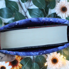 Load image into Gallery viewer, Pictured is a hand holding up a Purple Forest Guardian sleeve. Inside the sleeve we see a thick hardcover book.