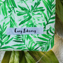 Load image into Gallery viewer, A close up of the Cozy Library tag is shown on the bottom right corner of a Green Tropical Palm book sleeve.