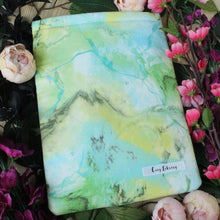 Load image into Gallery viewer, a book sleeve lays between flowers and leaves
