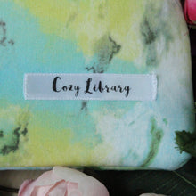 Load image into Gallery viewer, A close up of the Cozy Library tag is shown on the bottom right corner of a Sea Foam book sleeve.