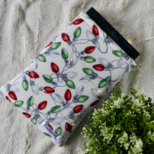 Load image into Gallery viewer, Old Fashioned Lights is pictured, holding a book. There's a plant in the bottom right corner of the picture. There are fairy lights wrapped around the book sleeve.