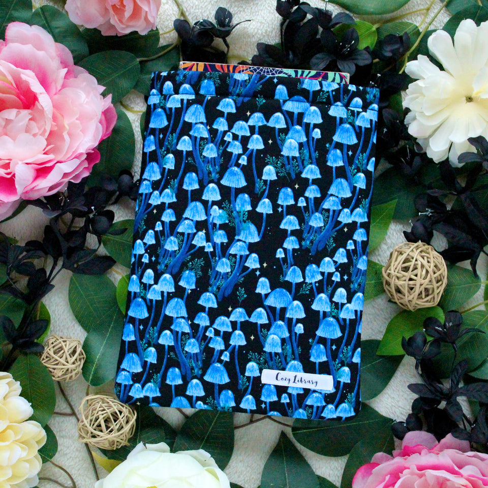 Moonlight Magic is pictured flat lay style, with a book coming out of the sleeve, there are various flowers in black, pink, and a yellowy-white placed throughout the photo.