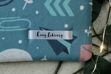 Load image into Gallery viewer, A close up of the Cozy Library tag is seen sewn into a Love Letters book sleeve.
