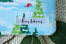 Load image into Gallery viewer, A close up of the Cozy Library tag is shown on the bottom right corner of a Rudolph&#39;s Christmas book sleeve.
