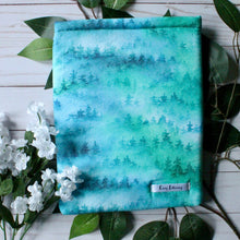 Load image into Gallery viewer, A medium-sized Forest book sleeve is pictured on top of leaves and white-washed wood background. One bunch of white flowers is down to the left of the picture and book sleeve.
