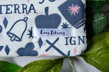 Load image into Gallery viewer, A close up of the Cozy Library tag is seen sewn into a Mystic Arts book sleeve.
