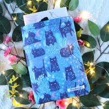 Load image into Gallery viewer, A paperback book titled Emergency Contact, by H.K. Choi is shown inside a blue version of Forest Guardian. There are cats in various positions. Seen with them is forest flora, and tiny long haired folk. Also in the picture are yellow and pink flowers, and leaves. A strand of fairy lights is laid down, giving the picture a fantasy-eqsue feel.
