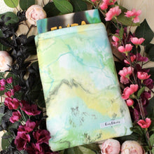 Load image into Gallery viewer, A book sleeve, holding a book, lays upon flowers and leaves.
