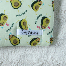 Load image into Gallery viewer, A close up of the Cozy Library tag is shown on the bottom right corner of a Avocardio book sleeve.
