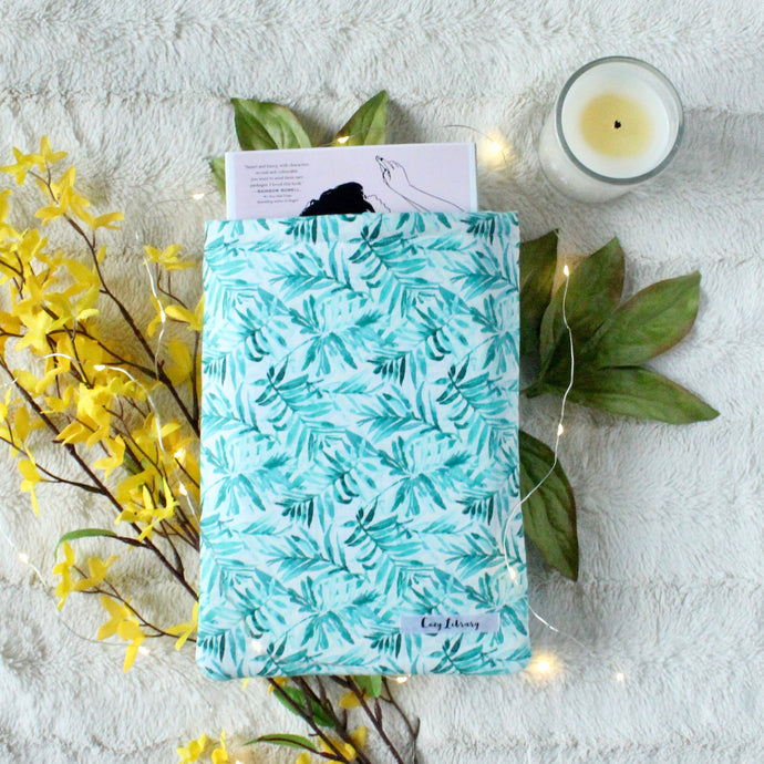 A small Blue Tropical Palm book sleeve is pictured. In the book sleeve is a paperback book titled 