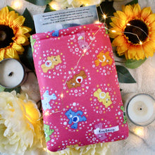Load image into Gallery viewer, A small-sized Care Bear book sleeve is shown. Halfway inside the sleeve is a paperback copy of Wintersong, by S. Jae-Jones.
