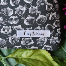 Load image into Gallery viewer, a close up of the Cozy Library tag sewn into the right hand corner of a Curioskitty book sleeve.
