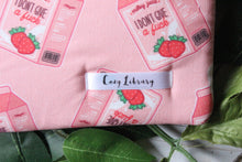 Load image into Gallery viewer, A close up of the Cozy Library tag is seen, sewn into a Sassy Juice book sleeve.

