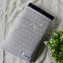 Load image into Gallery viewer, A small grey Frostine book sleeve is pictured. There is a plant in the bottom right corner of the picture, and there are fairy lights on top of the book sleeve.
