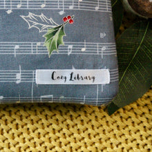 Load image into Gallery viewer, A close up of the Cozy Library tag is shown on the bottom right corner of a Carols book sleeve.
